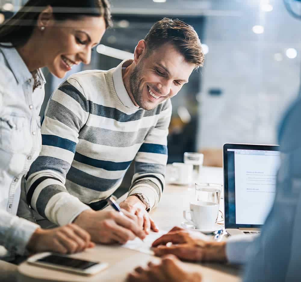 3 people work together around a table with a laptop
