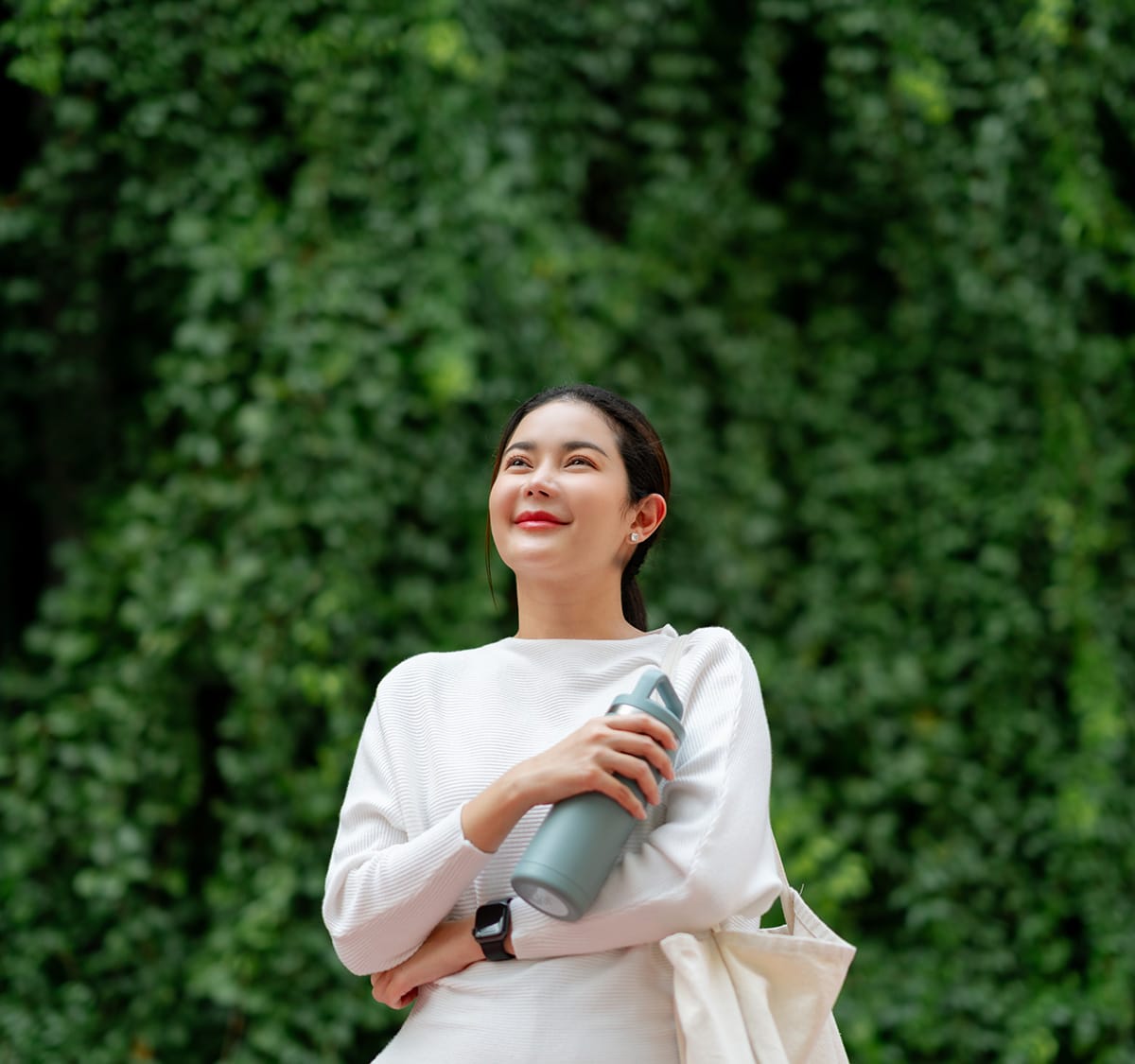 A woman holding a waterbottle and a bag smiles into the distance