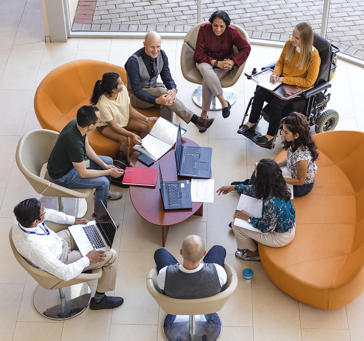 A group of nine people sit in a group in a casual indoor meeting space